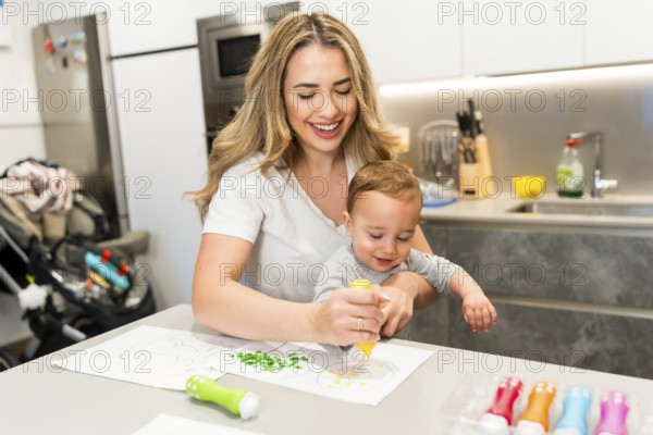 Happy mother and baby enjoying creative time, painting together in a bright, modern kitchen