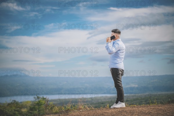 Handsome young man talking on the phone outdoors surrounded by nature. A person talking on the phone in a beautiful scenic viewpoint