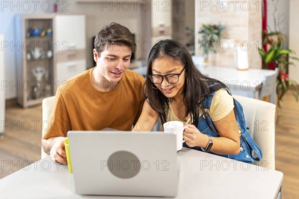 Multiethnic couple using laptop and drinking coffee at home, enjoying a relaxing moment together