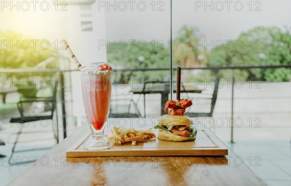 Delicious chicken burger with french fries and strawberry milkshake on restaurant table. Hamburger with french fries and strawberry milkshake on wooden table isolated