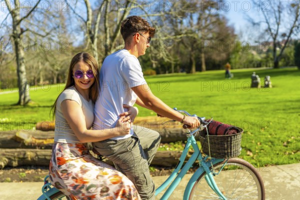 Romantic couple riding a bicycle together on a sunny day, enjoying the lush greenery of a vibrant park filled with joy and laughter