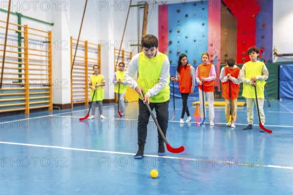 Group of preteen students wearing bibs, actively playing floorball during gym class in a lively school gymnasium