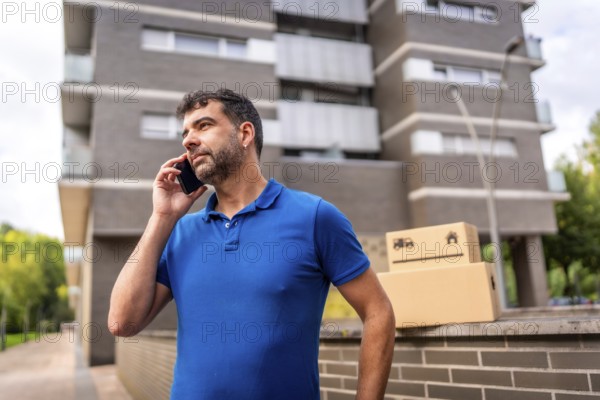 Delivery man talking to the mobile next to parcels to deliver outdoors