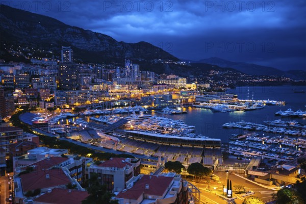 Aerial view of Monaco Monte Carlo harbour and illuminated city skyline in the evening blue hour twilight. Monaco Port night view with luxurious yachts