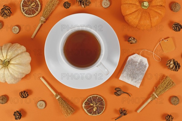 Cup of tea surrounded by seasonal fall decoration like pumpkins and orange slices on orange background