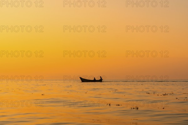 Fishing boat with a fisherman fishing in the orange sunset of Shkoder Lake in Shiroka. Albania