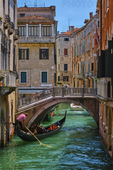 VENICE, ITALY, JULY 19, 2018: Narrow canal between colorful old houses with gondola boat with tourists and gonolier in Venice, Italy, Europe