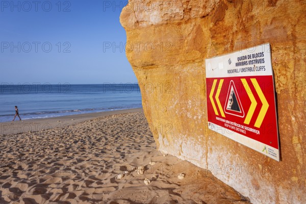 ROCKFALL UNSTABLE CLIFFS, KEEP A SAFE DISTANCE is written in English on a warning sign in Portugal on the cliffs of the Atlantic Ocean. Rocks and stones break out here again and again and injure people., Albufeira, Faro, Portugal, Europe