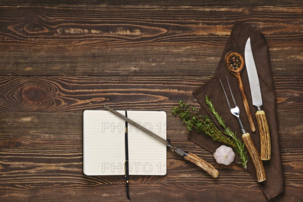 Vintage steak fork, knife and sharpener on wooden table next to notebook. Barbecue appliances and open notepad, food blogging and menu concept