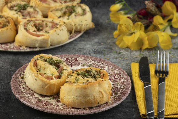 Baked dough snails with sausage and cheese on plates with cutlery and floral decorations in the background