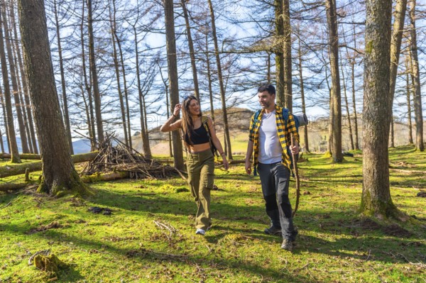 Hikers holding hands and carrying backpacks are walking through a sunny forest in springtime