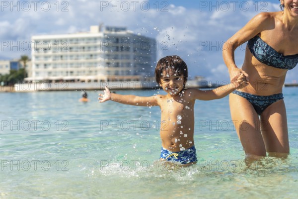 Mother and son holding hands and splashing in the clear turquoise water of estanys beach in mallorca, spain, enjoying summer holidays