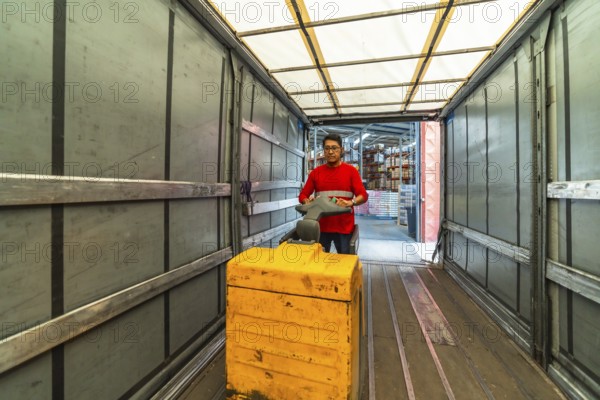 View from inside the vehicle of a male latin warehouse worker loading a truck using hydraulic hand pallet truck