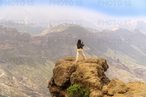 Woman photographing a scenic mountain range in gran canaria, canary islands, enjoying freedom and adventure in summer nature