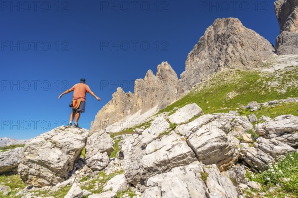 Tourist balancing on a rock formation with tre cime di lavaredo in the background, enjoying the breathtaking scenery of the dolomites in summer