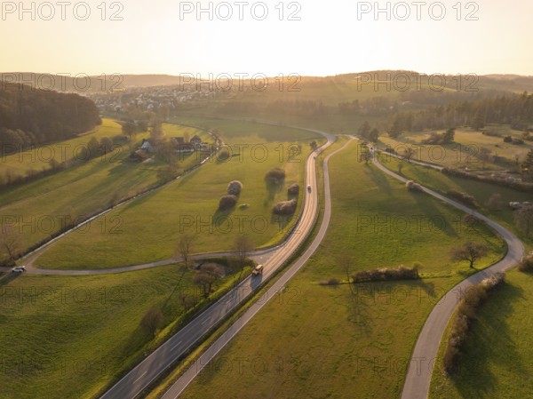 Winding country road through green fields and trees, under a warm sunset sky, Gechingen, district of Calw, Black Forest, Germany, Europe