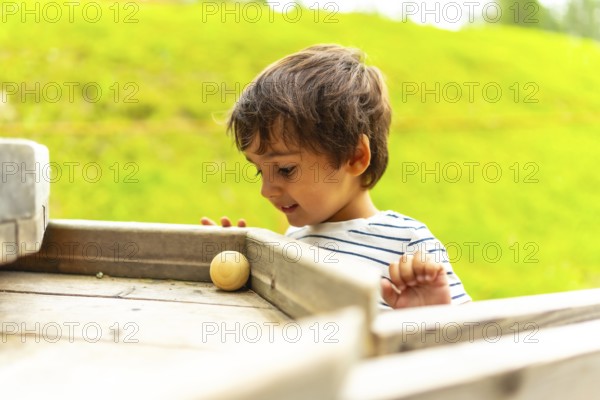 Happy child playing joyfully with a wooden ball on a vibrant playground structure during a sunny summer day, embracing fun and adventure