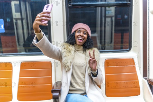 Cheerful young woman smiling and taking a selfie with a peace sign while enjoying her commute on the subway train in the city