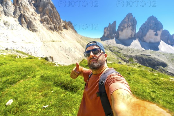 Hiker taking selfie and making thumbs up gesture with tre cime di lavaredo in background, dolomites, italy