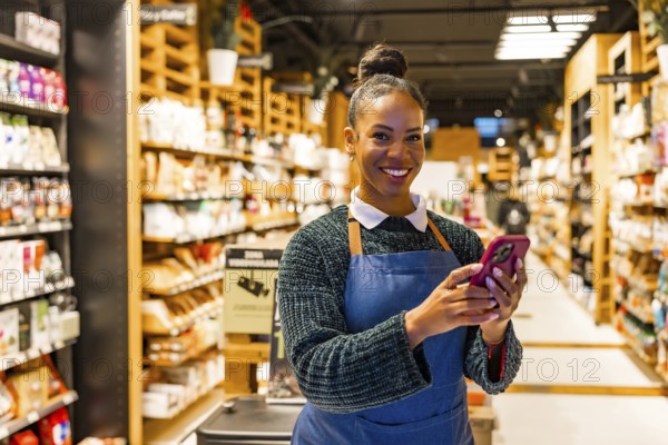 Smiling saleswoman using a smartphone in an organic supermarket with shelves full of natural and gluten free products