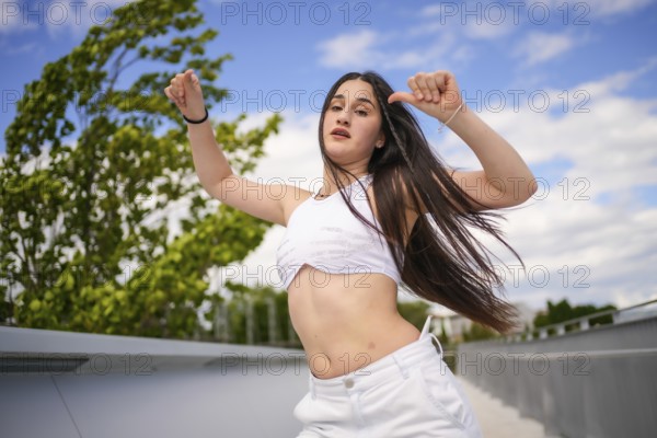 Young caucasian woman with arms raised and tousled hair dancing freestyle on an urban park