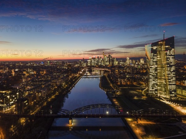 The lights in the offices of the European Central Bank (ECB) and in the skyscrapers of Frankfurt's banking skyline glow in the evening shortly after sunset. (Aerial view with a drone), Frankfurt am Main, Osthafen, Hesse, Germany, Europe