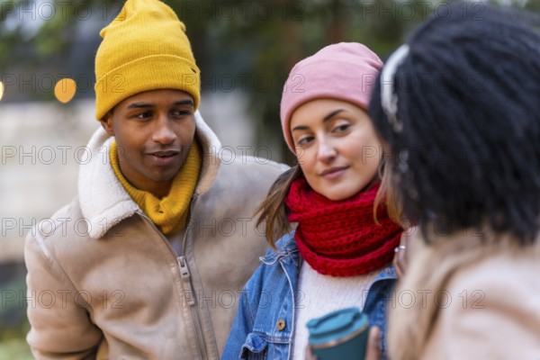 Three friends wearing winter clothes are enjoying a walk together in the city, sharing a conversation and a warm beverage