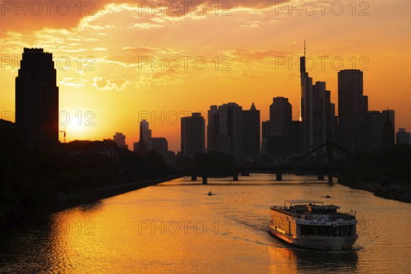 The sun sets behind the Frankfurt banking skyline as a PRIMUS LINE ship travels along the Main, Frankfurt am Main, Hesse, Germany, Europe