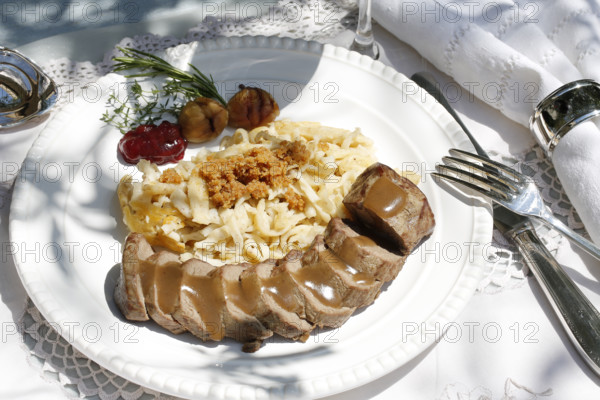 Swabian cuisine, roast venison with spaetzle, chestnuts and breadcrumbs, breadcrumbs, saddle of venison arranged on a plate, gravy, game dish, meat, main course, gravy, cutlery, knife, fork, grandmother's kitchen, regional, home cooking, typical Swabian, traditional cuisine, festive tablecloth, food photography, studio, Germany, Europe