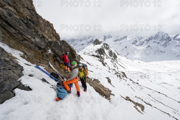 Three mountaineers at the ski depot of Piz Laviner, view of mountain panorama in wintry mountain landscape with dramatic clouds, Grisons Haute Route, Albula Alps, Rhaetian Alps, Grisons, Eastern Switzerland, Switzerland, Europe