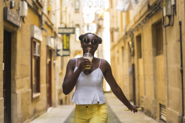 Cool african young woman drinking juice while walking happily in a street