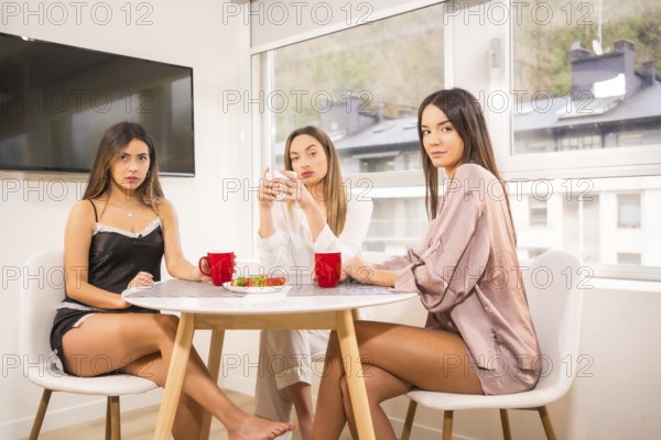 Lifestyle of Caucasian friends on vacation in a hotel having breakfast, dressed in nightwear, drinking coffee and posing for the camera