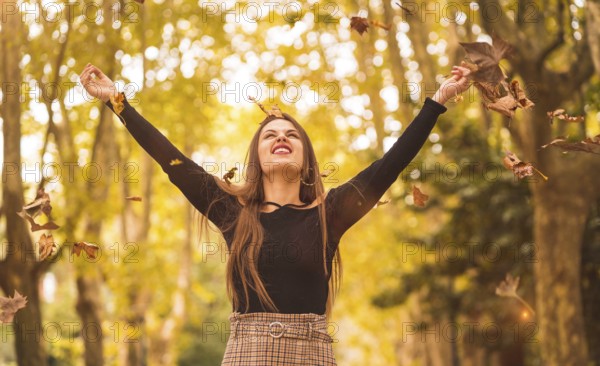 Portrait of a woman in autumn in a forest with brown leaves at sunset in a city park, throwing leaves at sunset