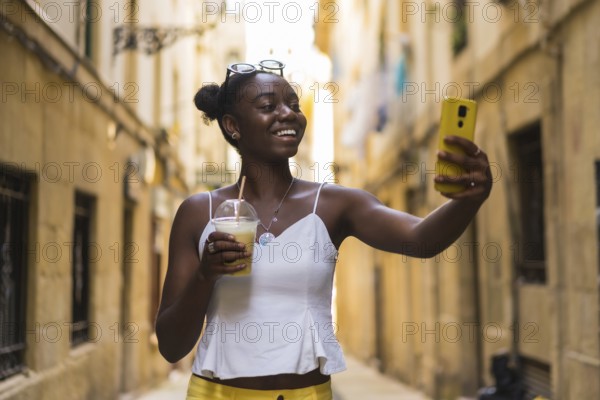 Smiling young african american woman talking selfie showing a delicious milkshake in the city street