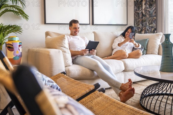 Technological weekend for a couple in casual comfortable clothes sitting in their sofa