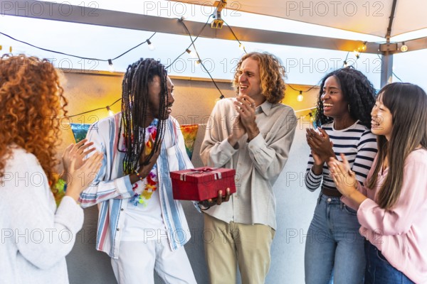 African man thanking his multi-ethnic friends for the birthday gift they gave him during a party on a terrace