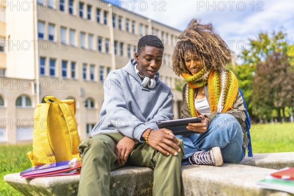 Young male and female diverse university student using tablet while sitting on steps outdoors at the university campus