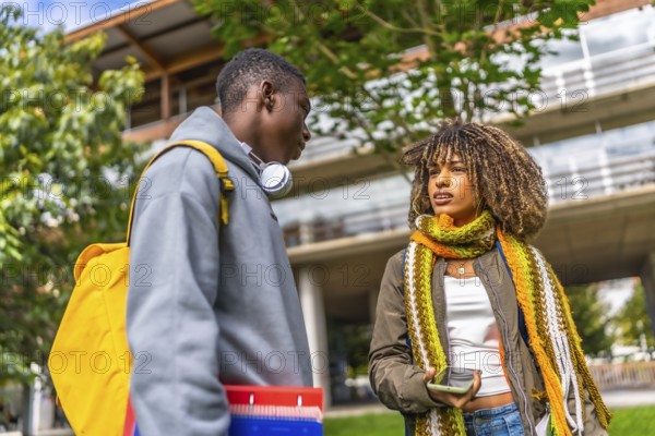 Low angle view photo of two diverse students talking and sharing mobile standing outside the university