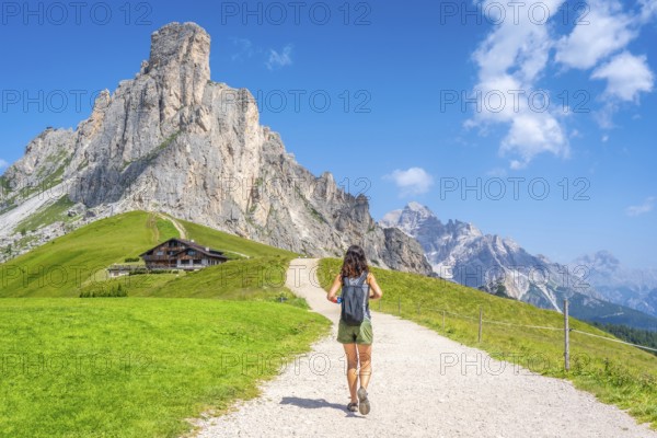 Female tourist walking on a gravel path enjoying the view of the nuvolau peak and the mountain shelter near giau pass in the italian dolomites