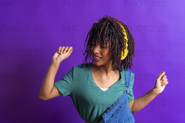 Happy young woman with yellow headphones dancing and enjoying music on a vibrant purple background, expressing joy and carefree attitude