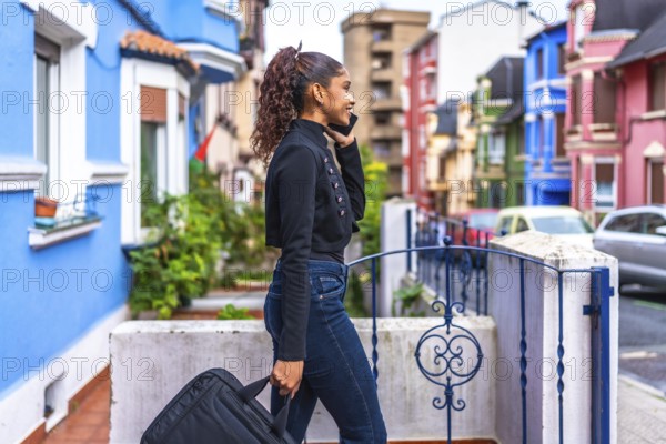African american casual businesswoman carrying laptop bag and talking to the mobile phone leaving home along a colorful street