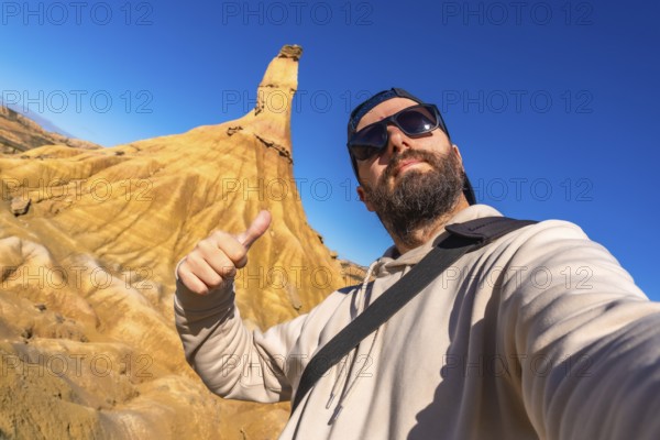 Tourist making thumbs up sign enjoying the view of the geological formations in bardenas reales desert, navarre, spain