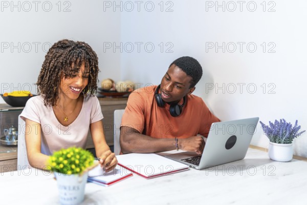 Young black entrepreneurs working from home using laptop and taking notes, collaborating on a project