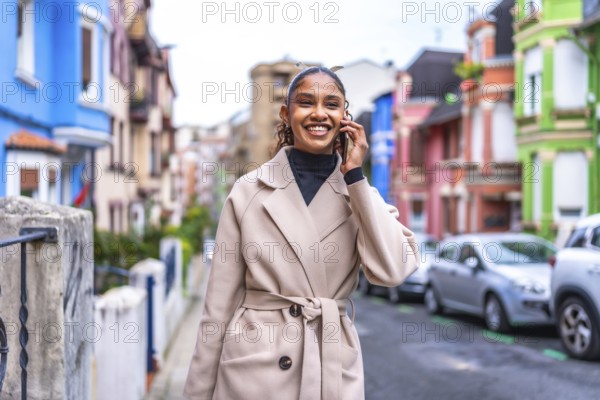 Smiling african businesswoman talking to the mobile phone walking along a colorful street in the city in autumn