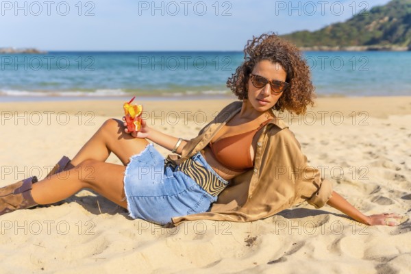 Sensual woman in denim summer clothes and bikini leaning on beach enjoying tropical fruit