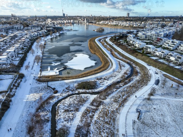 Dortmund, North Rhine-Westphalia, Germany, Phoenix Lake in winter with snow, renaturalised Emscher in front. The river was transformed into a near-natural body of water, flood protection and biodiversity through newly designed floodplains. A former industrial wasteland of 99 hectares was transformed into residential, work and leisure areas and 24 hectares of lake surface. In the event of heavy rainfall, the lake acts as a rainwater retention basin. Following the construction of a parallel sewer, the Emscher is now free of wastewater, having previously been an open, above-ground wastewater sewer, combined sewer with surface water and wastewater. The Phoenix Lake, a showcase project for structural change, is an artificial lake on the site of the former Phönix Ost steelworks in Dortmund's Hörde district, Europe