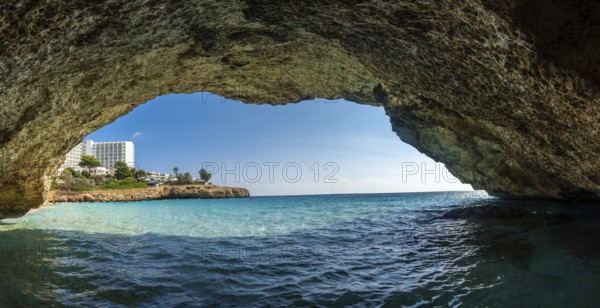 Capturing a breathtaking view of turquoise waters and a resort in cala domingos, mallorca, from inside a cave along the coastline