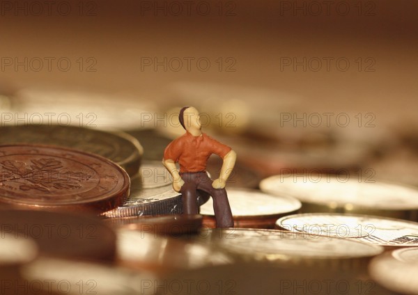 Miniature man sitting among euro coins, North Rhine-Westphalia, Germany, Europe