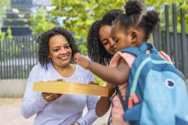 African schoolgirl playing with toys in a park with her mother and grandmother