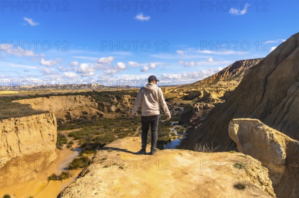 Tourist standing on cliff edge, admiring the geological formations and vast landscape of bardenas reales desert in navarre, spain, under a beautiful blue sky